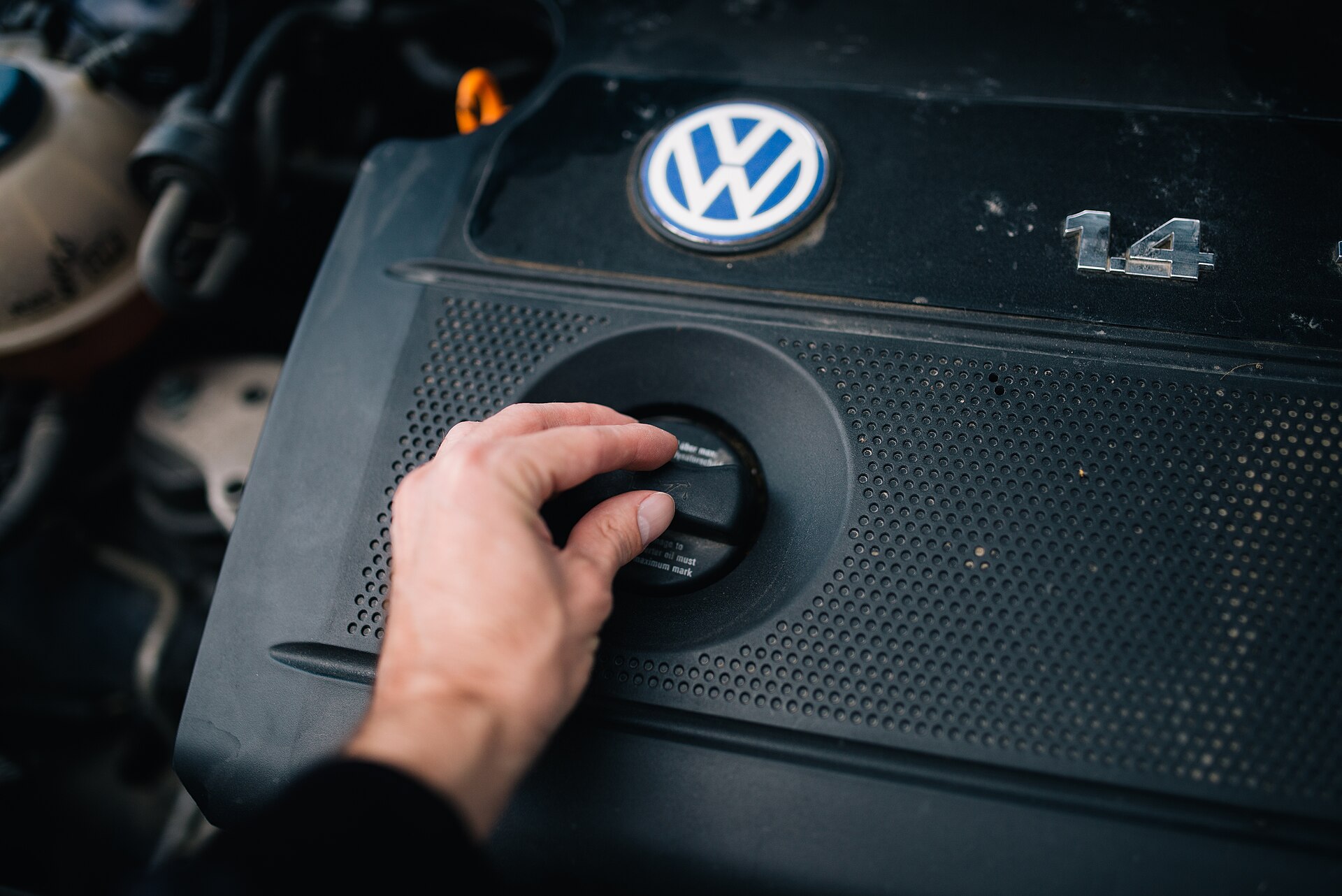 Een hand draait aan de olievuldop van een motor