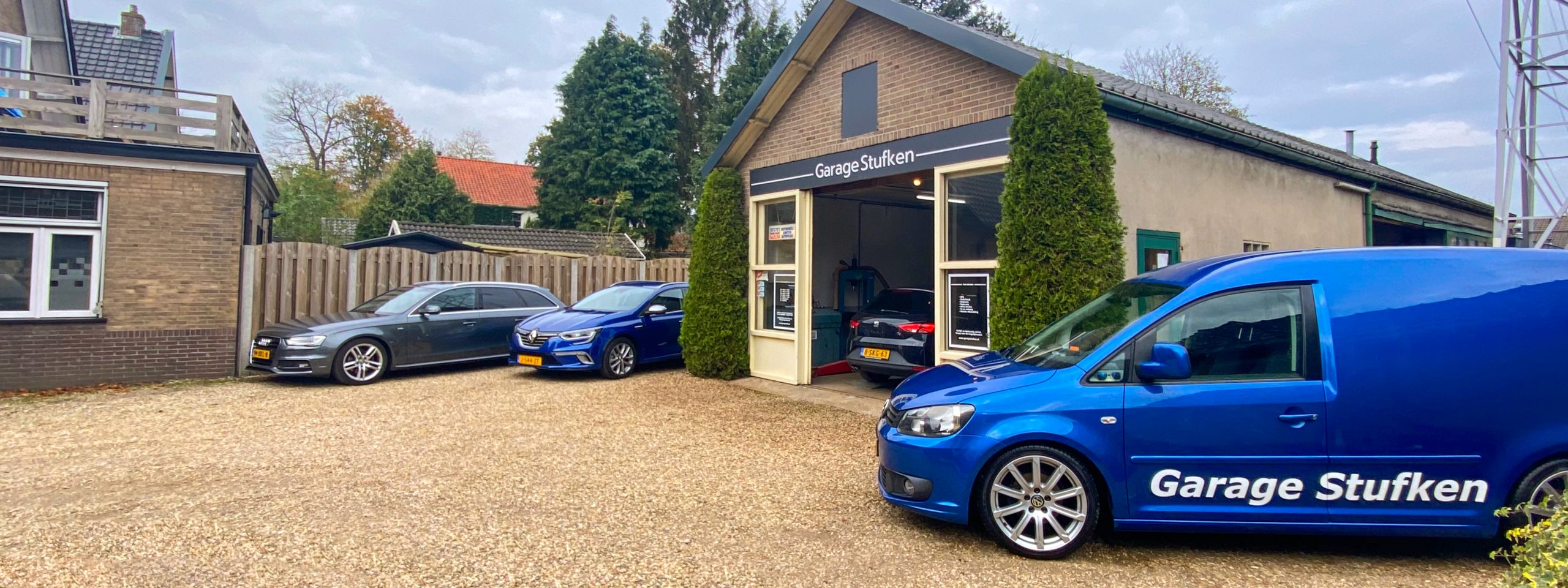 Garage Stufken aan de Dorpstraat in Beekbergen, met drie auto's op het grind en de blauwe Caddy met belettering voor de deur