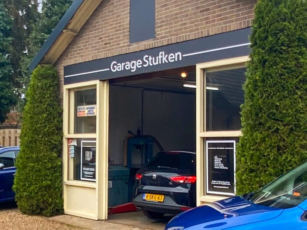 De open inrijpoort van Garage Stufken met een auto op de brug en het naambord erboven