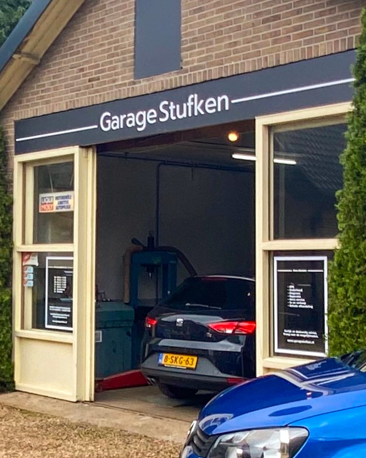 De open inrijpoort van Garage Stufken met een auto op de brug